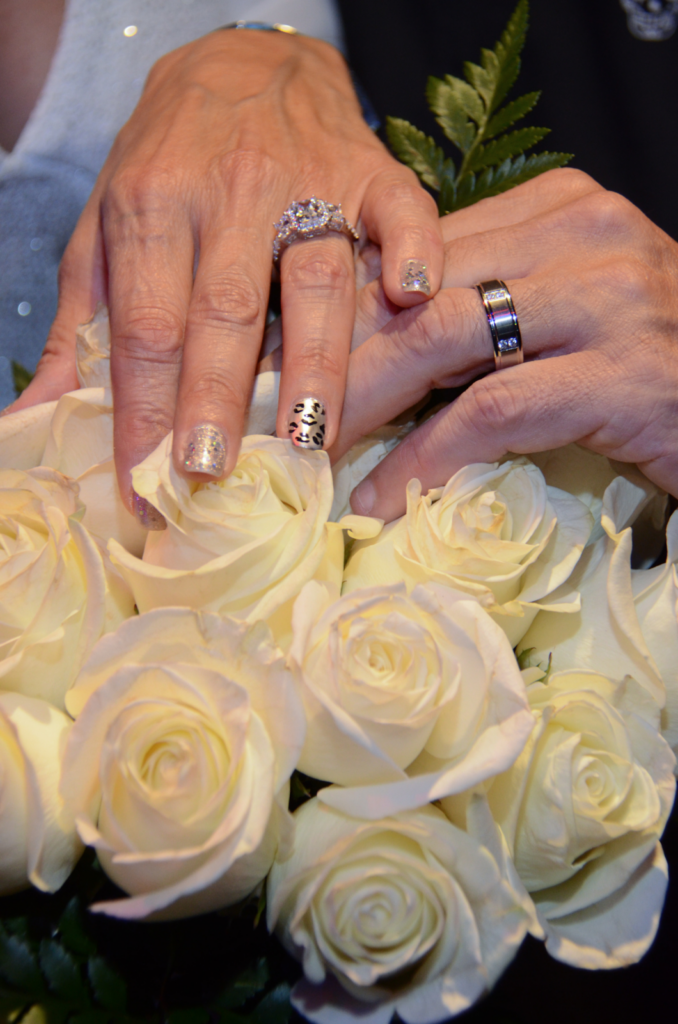 A bride and groom's hands placed on top of a bouquet of roses as they show off their wedding rings.